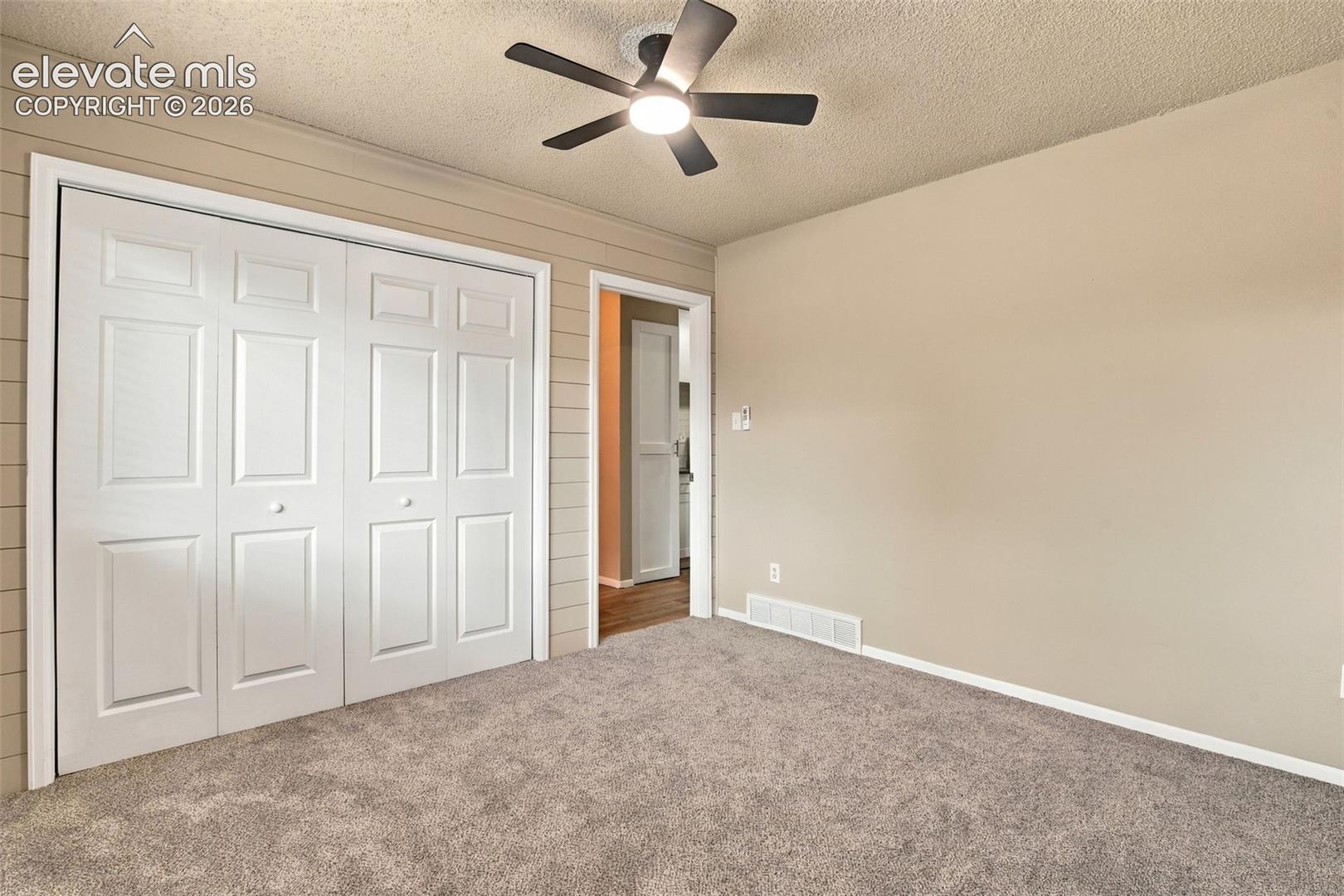 Room featuring neutral carpeting, horizontal wall paneling, a ceiling fan with integrated lighting, and a white paneled closet door