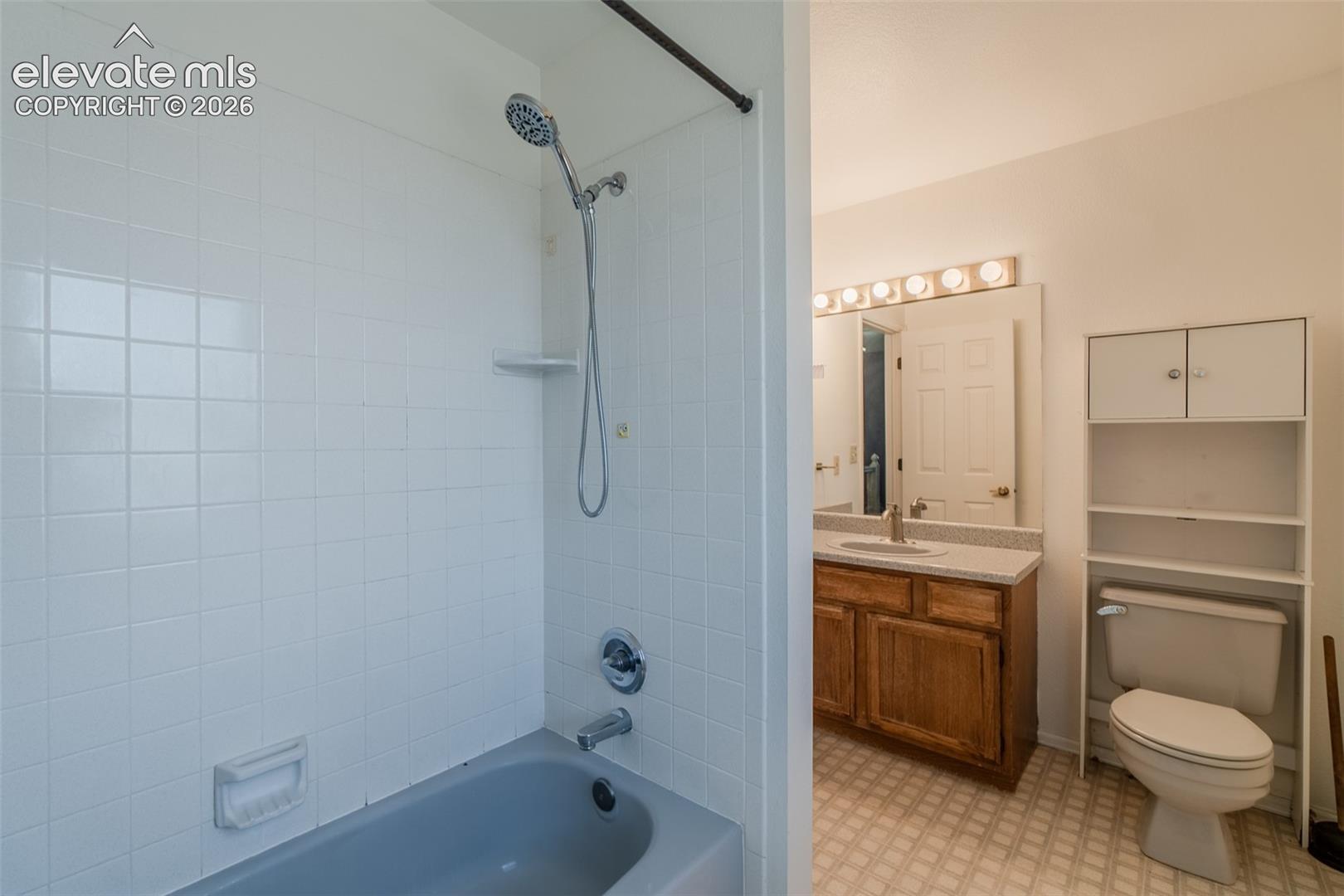 Full hallway bathroom featuring a shower-tub combination with white tile surround, vanity with wood-finish cabinetry, a single sink, and overhead illumination, and a toilet