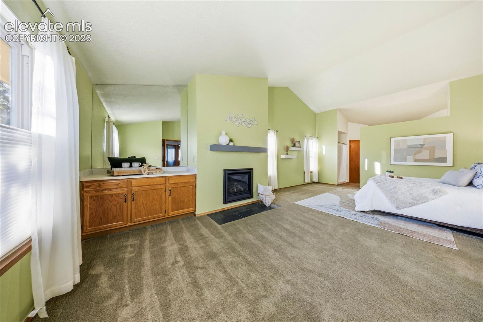 Vaulted ceilings, fireplace with a mantel, built-in cabinetry, mirror-accented vanity, and carpeted flooring