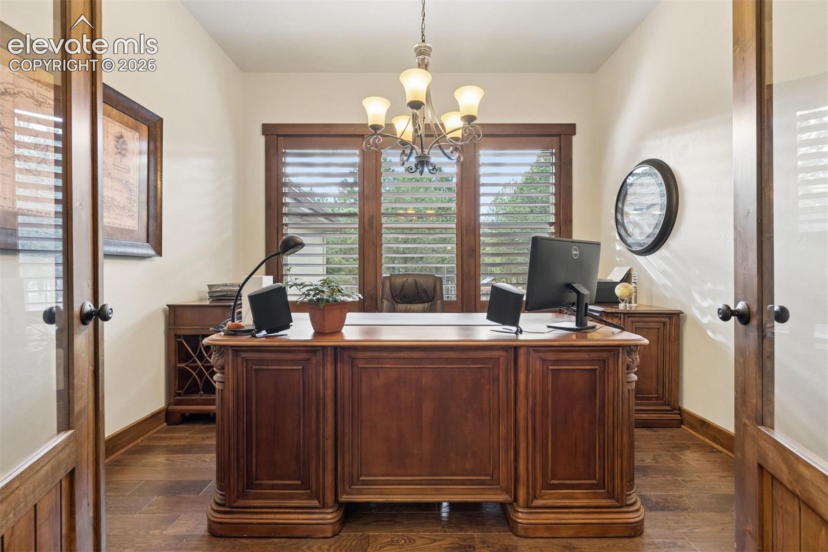 Wood-finish flooring, French doors with glass panes, wood-framed windows with plantation shutters, and a multi-arm chandelier