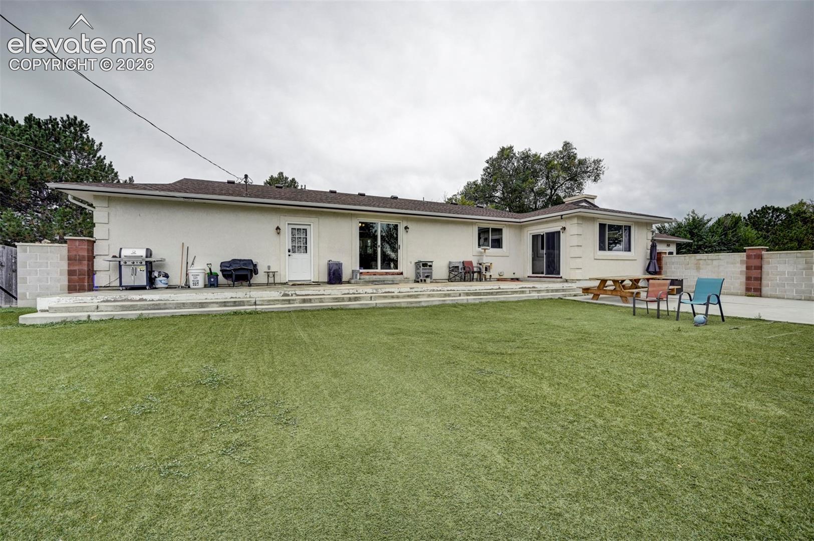 Expansive artificial turf lawn with a multi-level concrete patio, stucco exterior, and sliding glass doors
