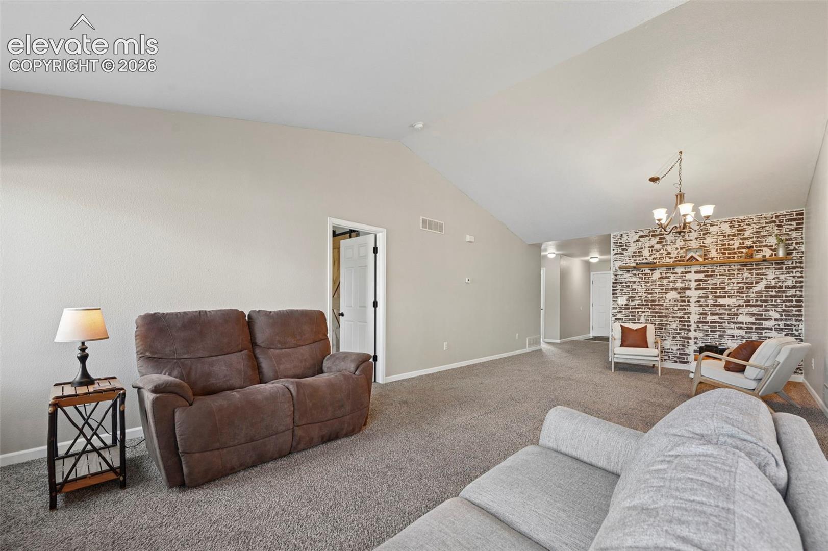 Vaulted ceilings, exposed brick accent wall, built-in wooden mantel, and multi-arm chandelier