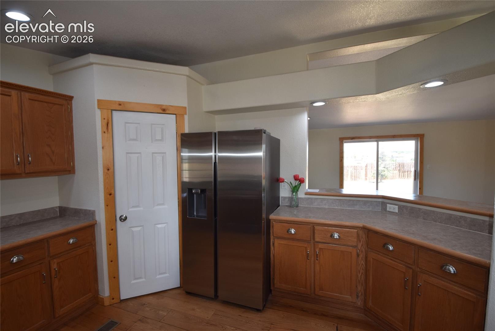 Kitchen featuring wood-finish flooring, wood cabinetry with silver-tone hardware, a stainless steel refrigerator, and a built-in breakfast bar with a laminate countertop