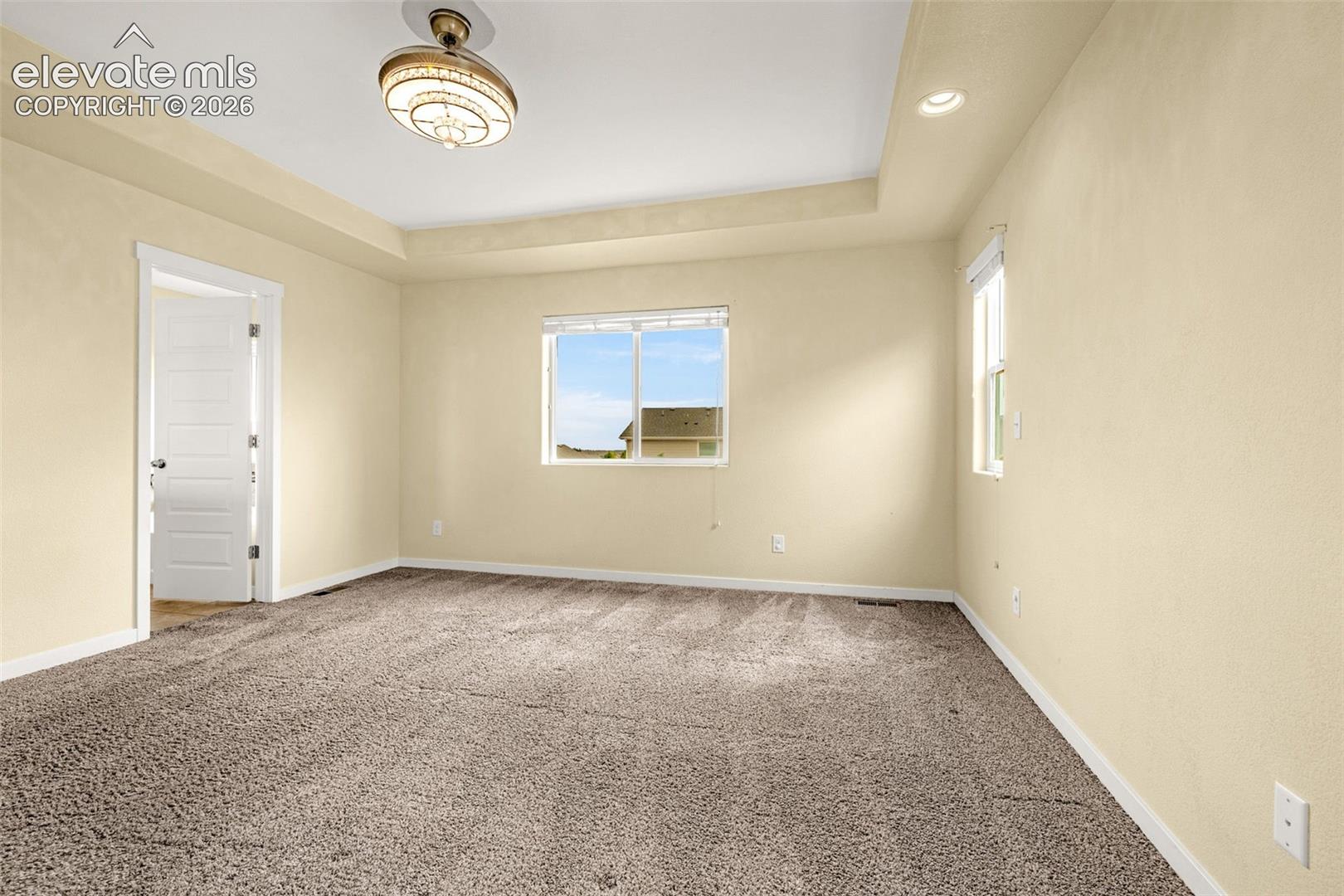 Tray ceiling with recessed lighting and a central ceiling fixture, wall-to-wall carpeting, and multiple windows