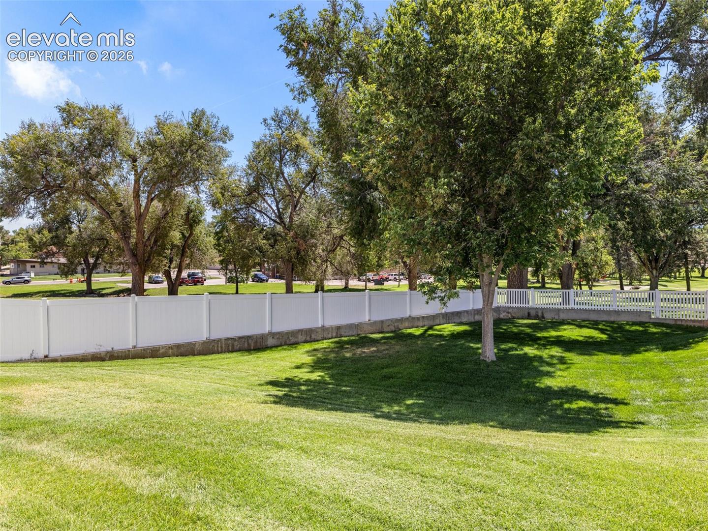 Expansive green lawn with mature trees and a white privacy fence