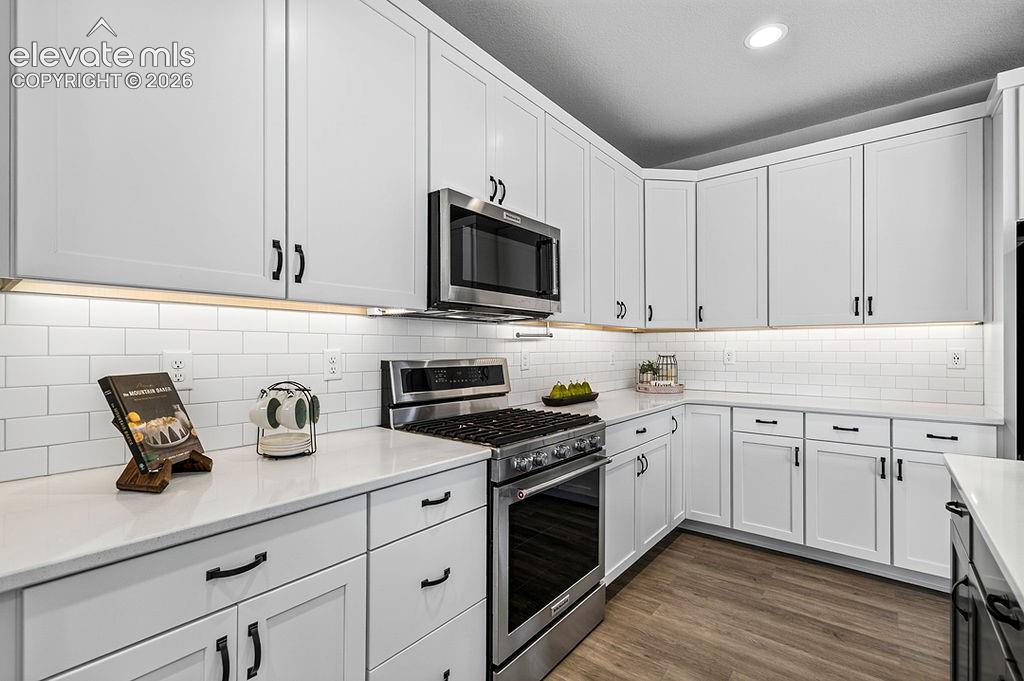 Contemporary kitchen featuring white cabinetry with matte black hardware, stainless steel appliances, subway tile backsplash, and white countertops