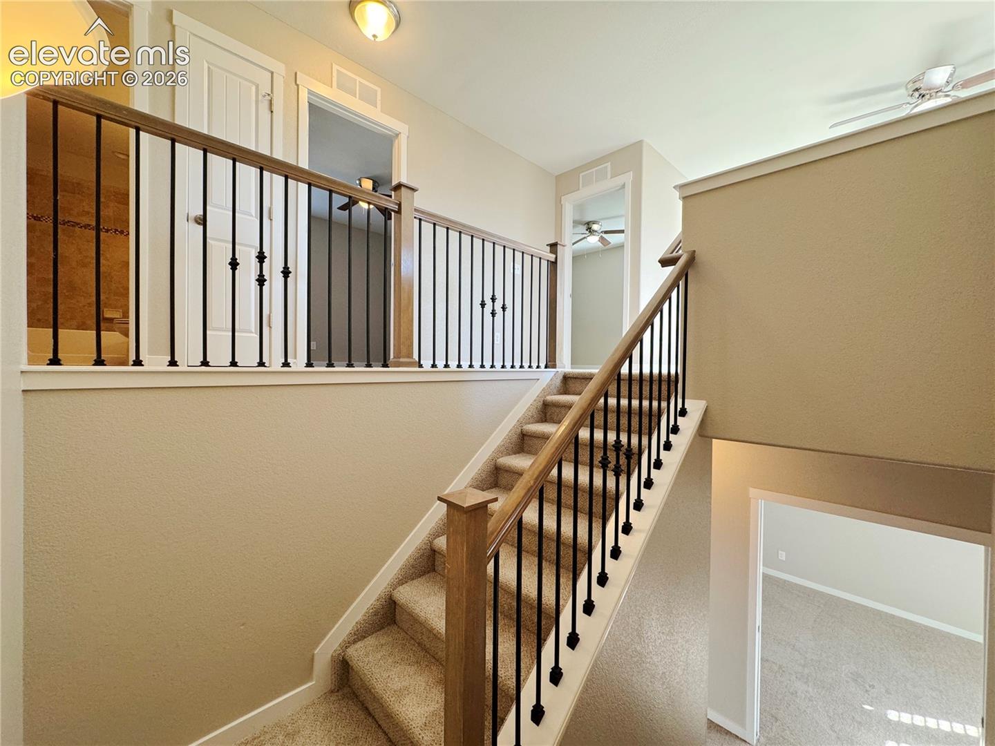 Staircase featuring neutral carpeting, a wooden handrail, and decorative black metal balusters