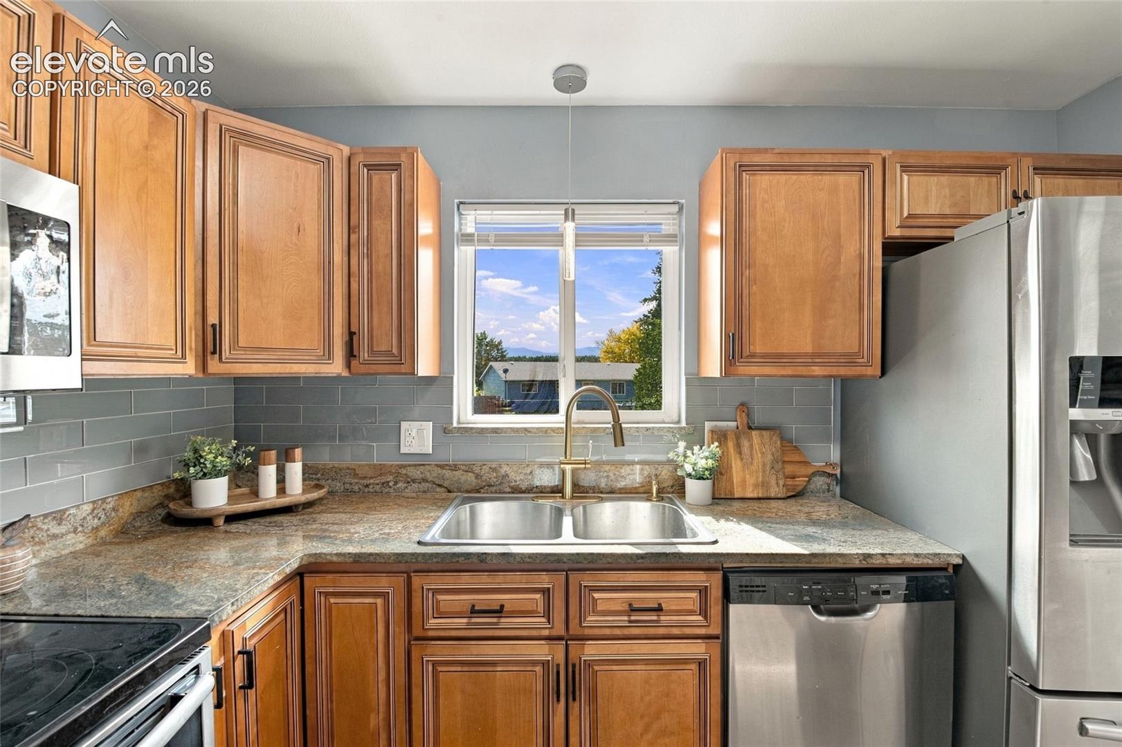 Kitchen featuring natural-finish wood cabinetry, stone-surface countertops, subway tile backsplash, stainless steel appliances, and a dual-basin sink with a gooseneck faucet