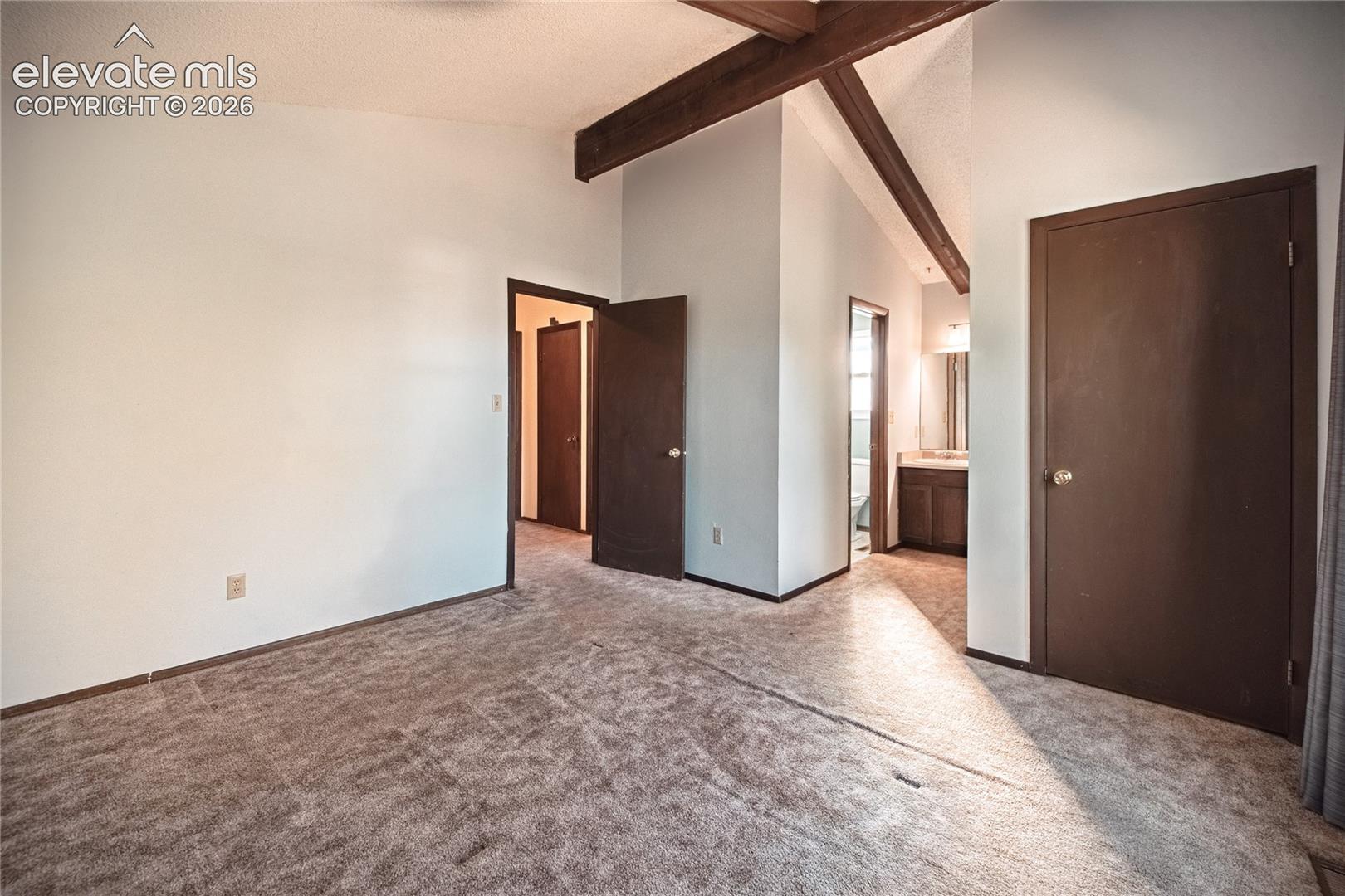 Vaulted ceilings featuring exposed wood beams, wall-to-wall carpeting, and solid-core interior doors