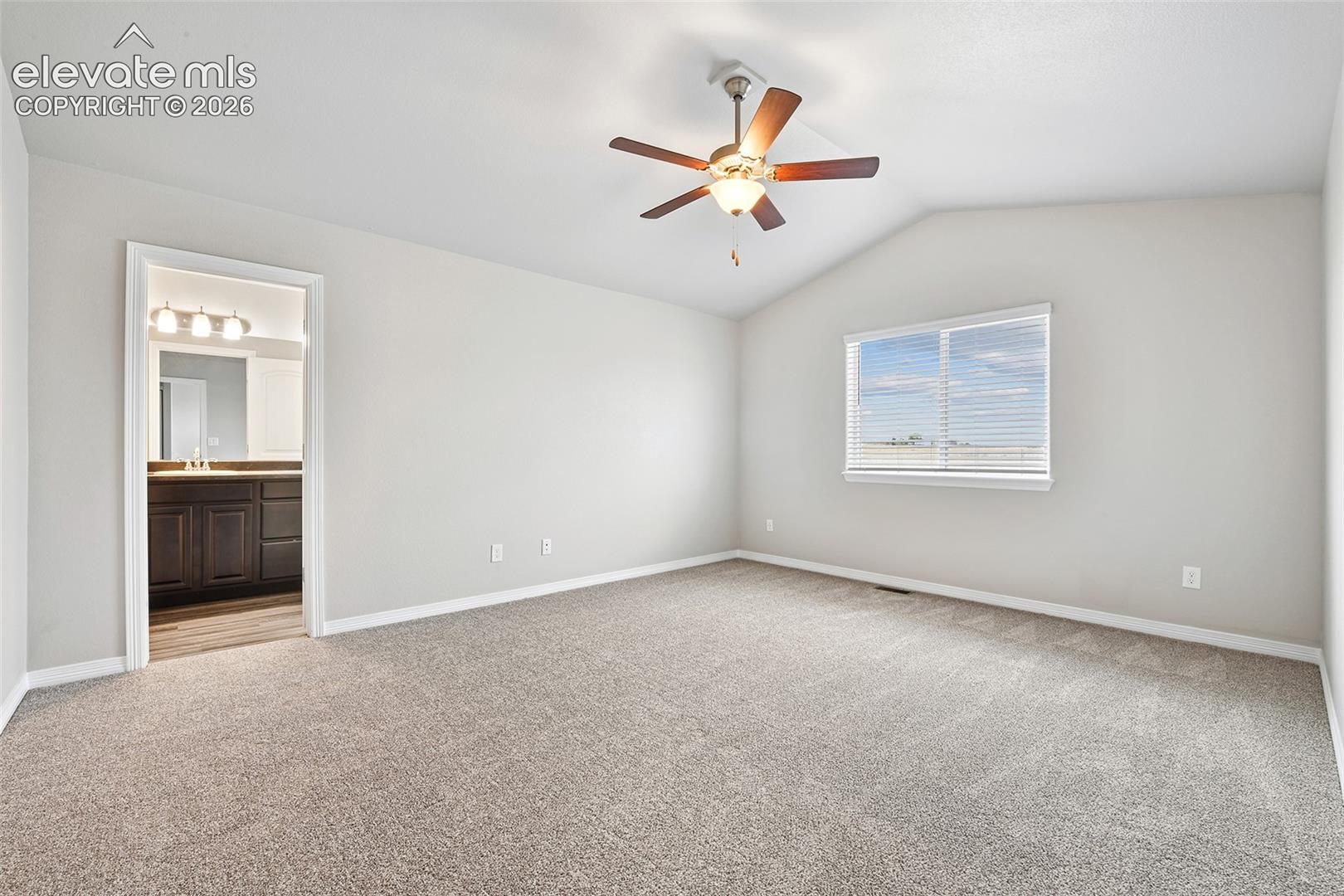 Vaulted ceilings featuring a central light-integrated ceiling fan, neutral wall-to-wall carpeting, and a dual-pane window