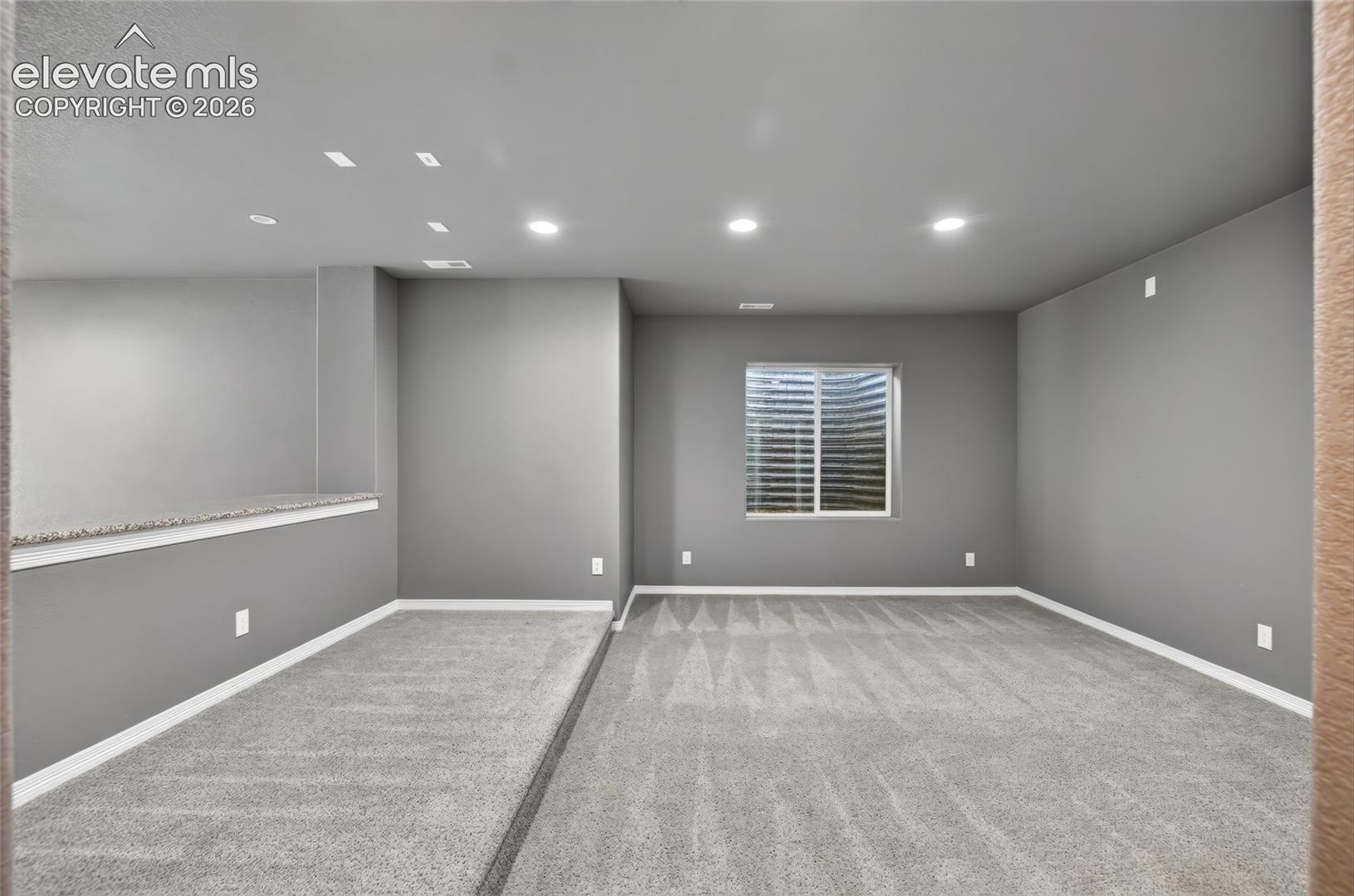 Recessed lighting, light gray wall color, gray patterned carpeting, white window trim, and white baseboards
