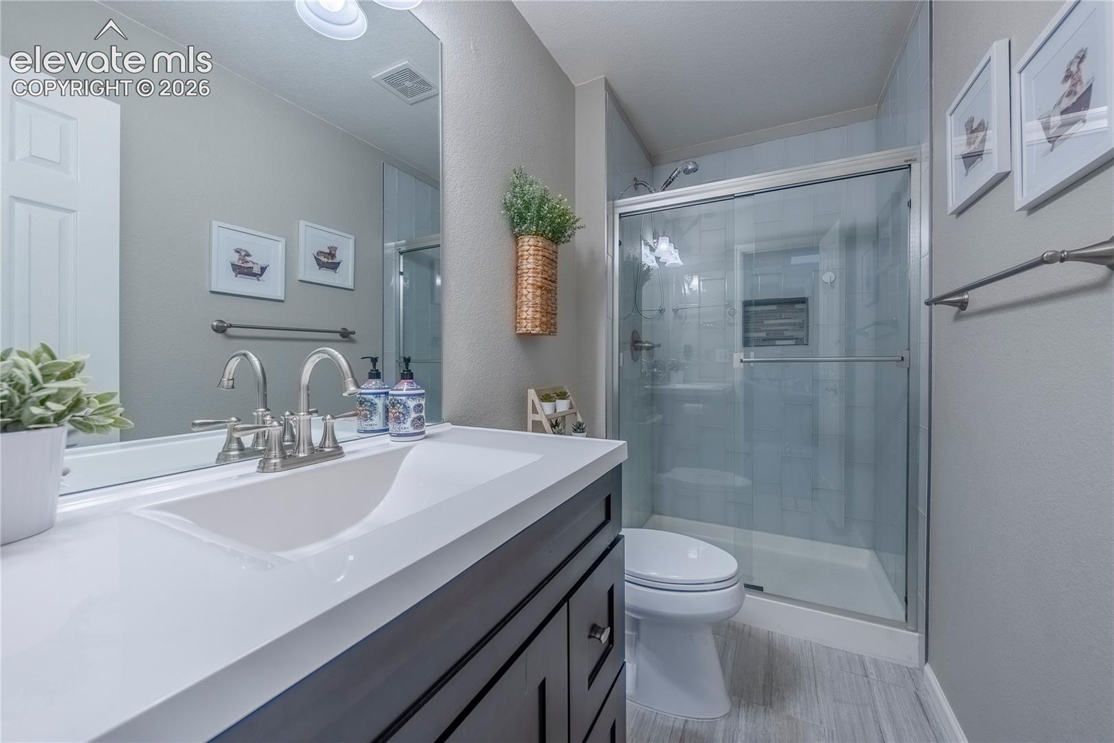 Bathroom featuring a dark-finish vanity with a light-toned countertop, integrated rectangular sink, brushed-nickel faucet, and a glass-enclosed shower with a built-in recessed shelf