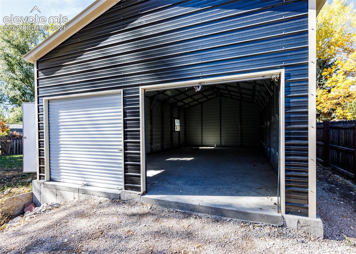Detached garage featuring black corrugated metal siding, a concrete foundation, a roll-up bay door, and an open-entry bay