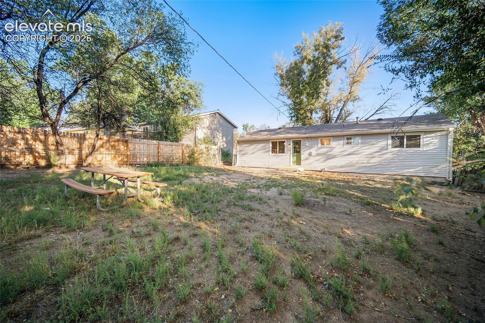 Expansive sloped yard featuring mature trees and a wood picket fence