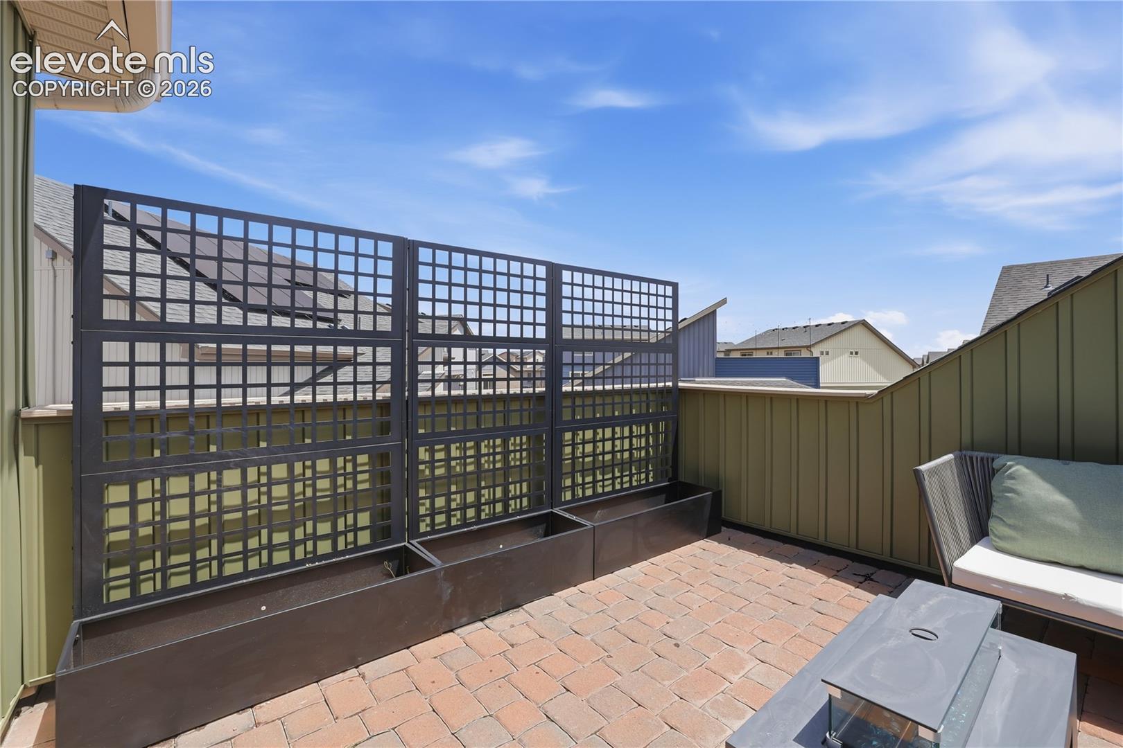 Rooftop patio featuring brick paver flooring, a dark metal trellis system with integrated planter boxes, and olive green siding