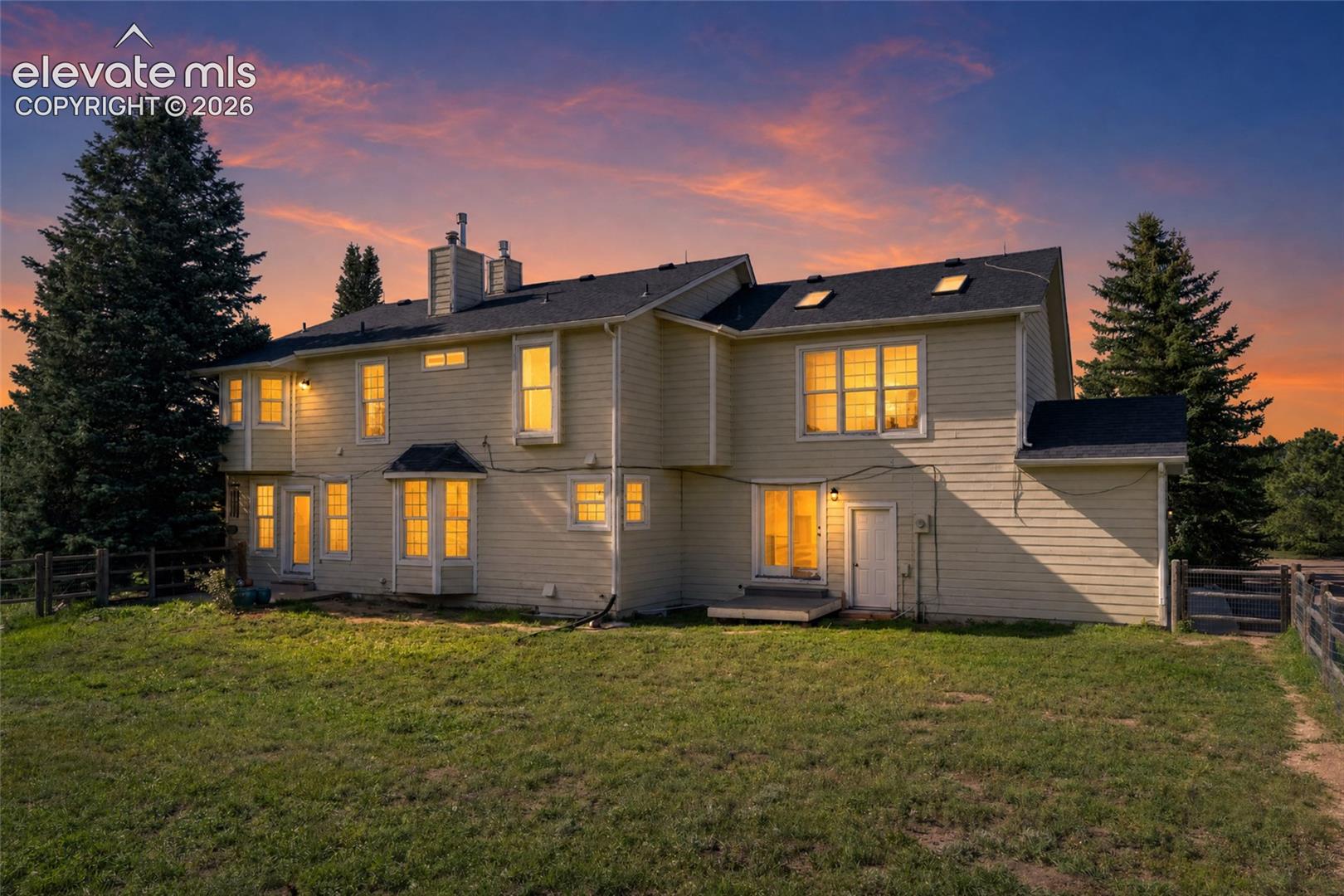 Rear exterior featuring multiple windows, skylights, and a wood fence