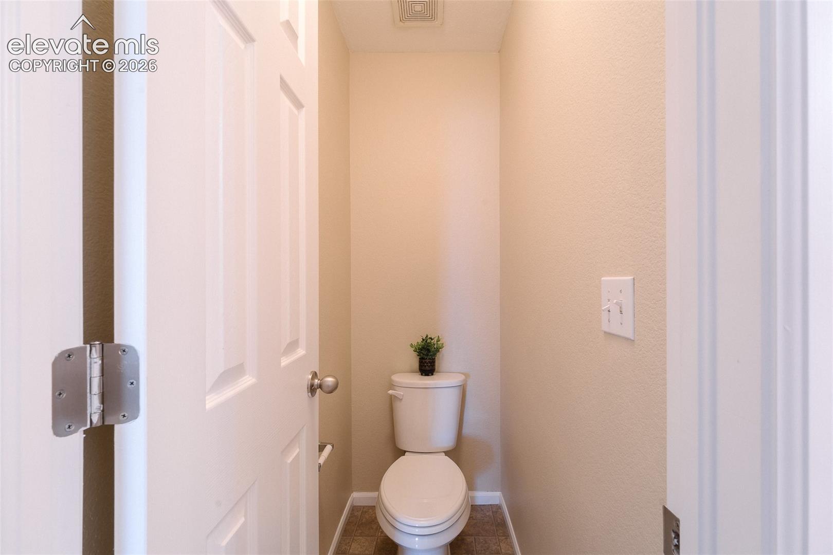 Enclosed space featuring a two-piece toilet, paneled interior door with metal hinges, and neutral wall tones