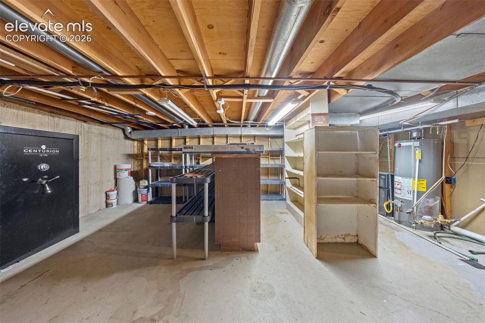 Unfinished lower level featuring exposed wood joist ceilings, concrete flooring, poured concrete foundation walls, and an integrated water heater