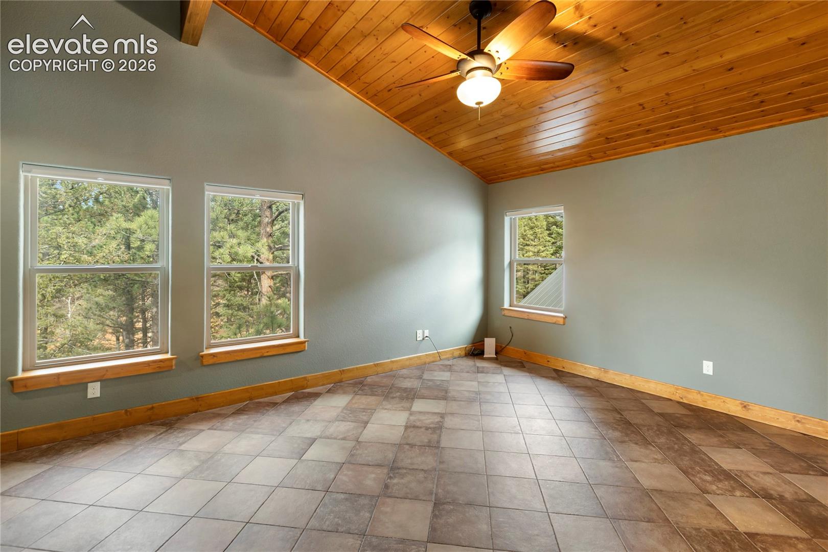 Vaulted ceilings with exposed wood-plank paneling, large-format tile flooring, natural wood trim, and multiple windows