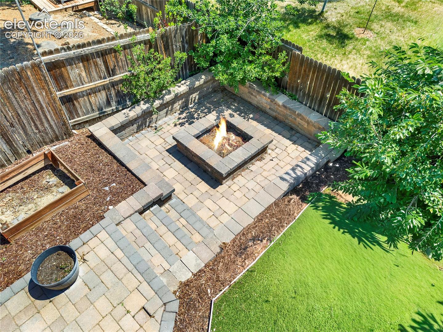 Custom paver patio featuring a built-in stone fire pit, tiered stone retaining walls, and wooden perimeter fencing