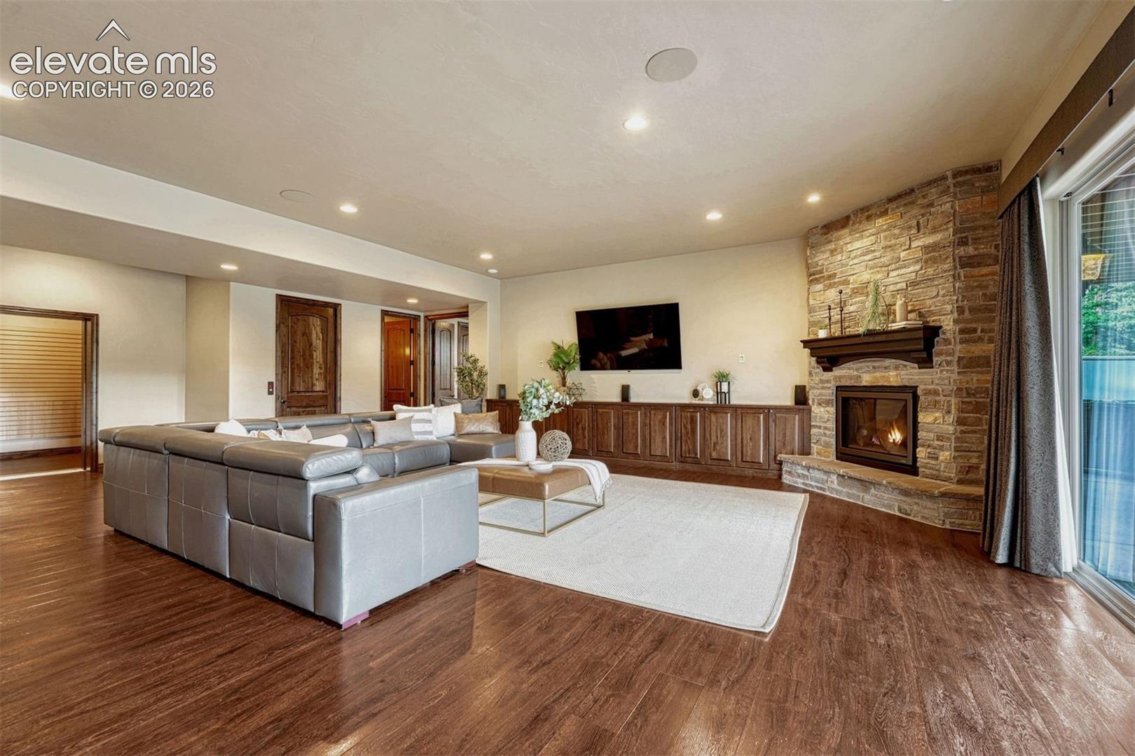 Wood-finish flooring throughout, stone-clad fireplace with mantel, built-in wood cabinetry, recessed lighting, and expansive sliding glass doors