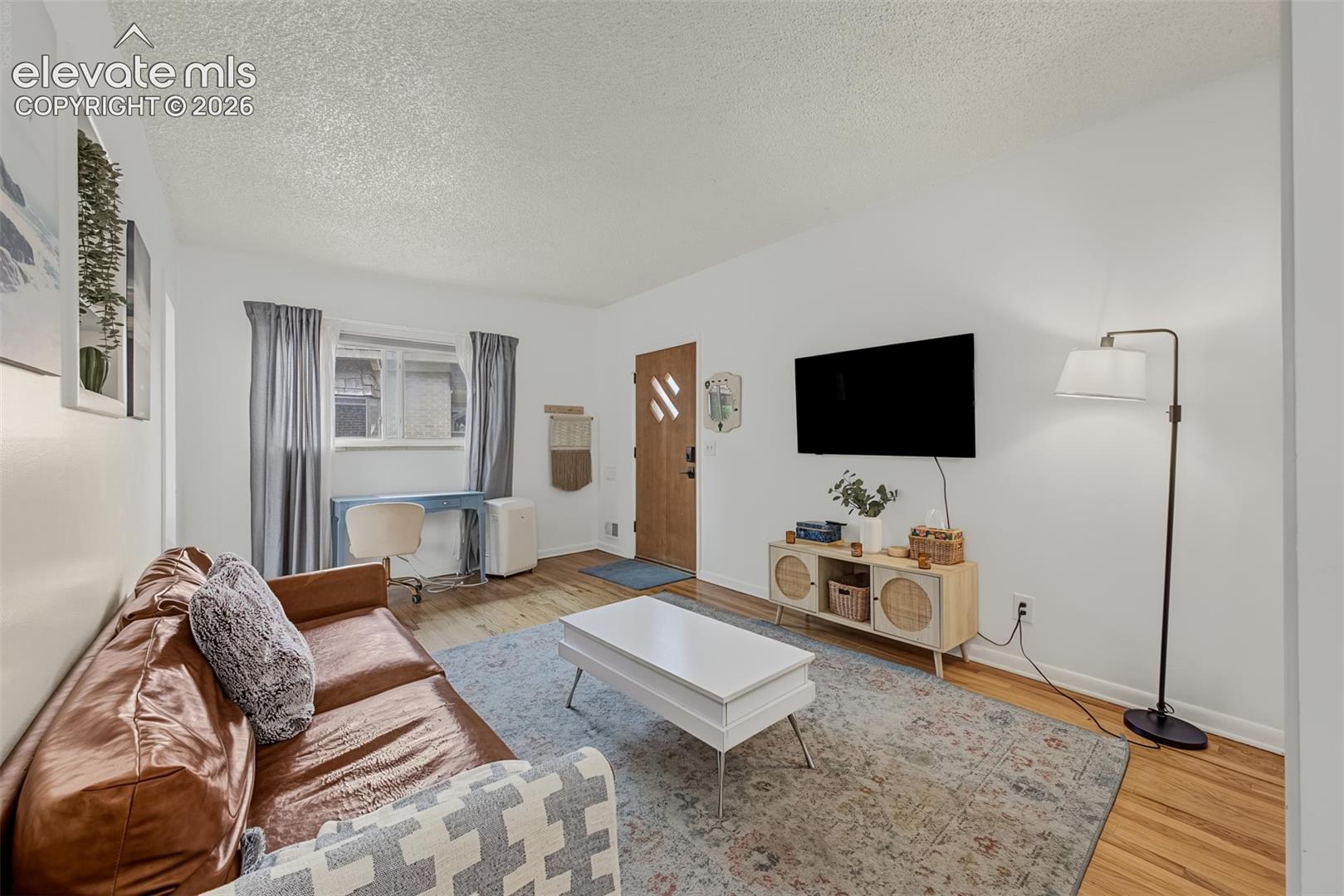 Living space featuring wood-finish flooring, textured ceiling, neutral wall color, and a wood-finish exterior door with a geometric window inlay