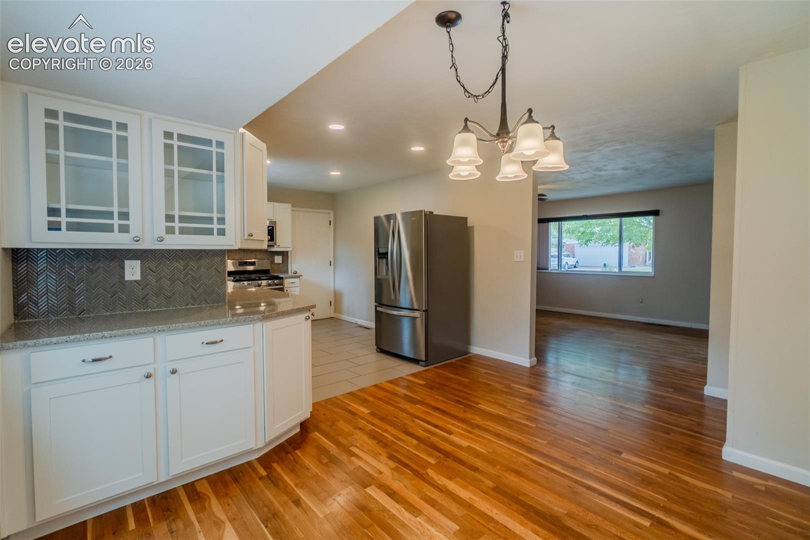 Kitchen featuring white cabinetry, glass-front upper cabinets, patterned tile backsplash, light-toned countertops, and stainless steel appliances