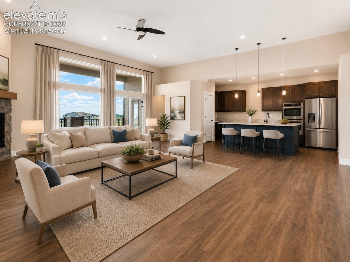 Virtually Staged Spacious open-concept living area featuring wood-finish flooring, a stone fireplace with wood mantel, and large windows