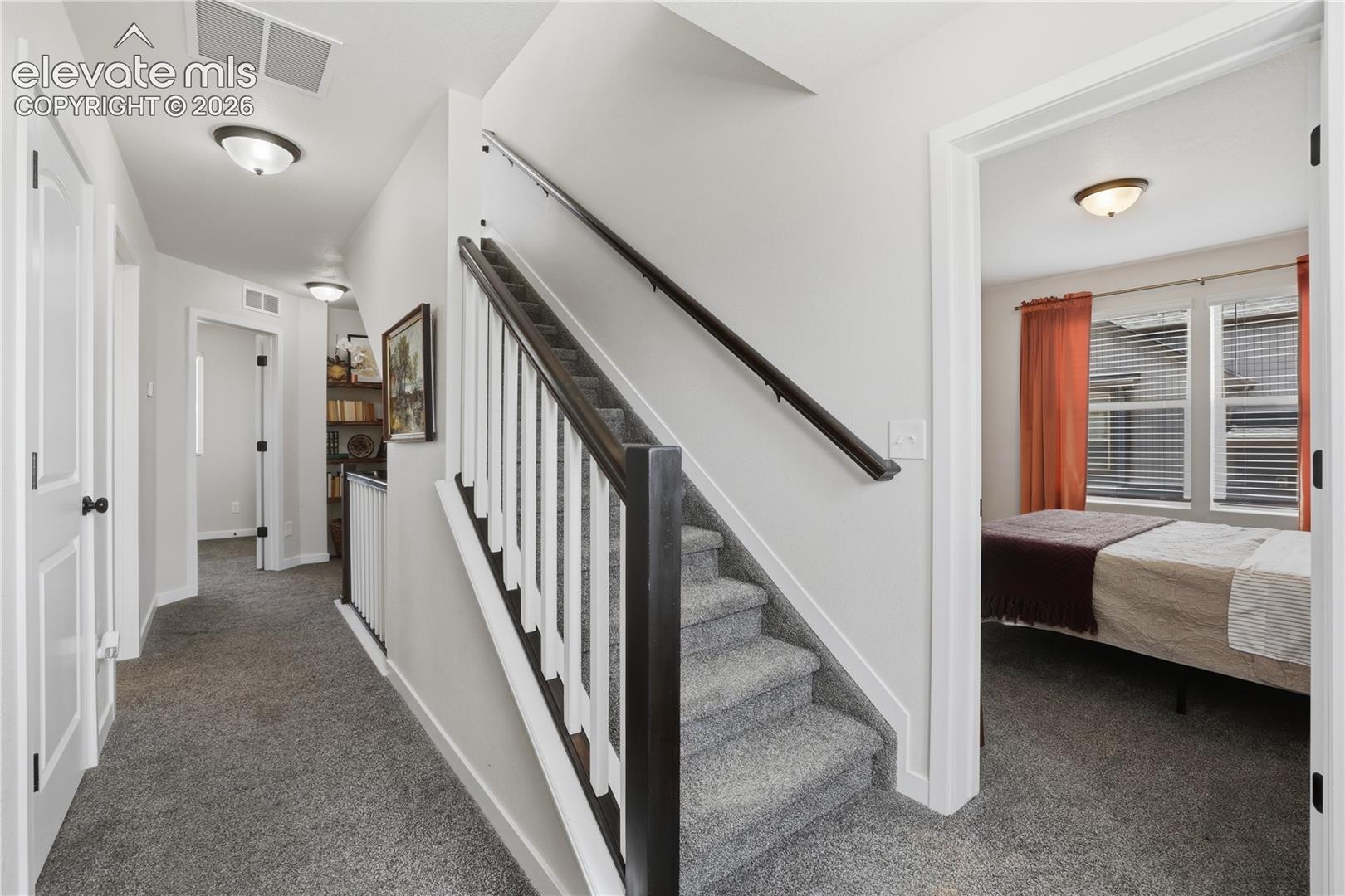 Interior staircase with carpeted treads and dark wood banister, featuring white spindles