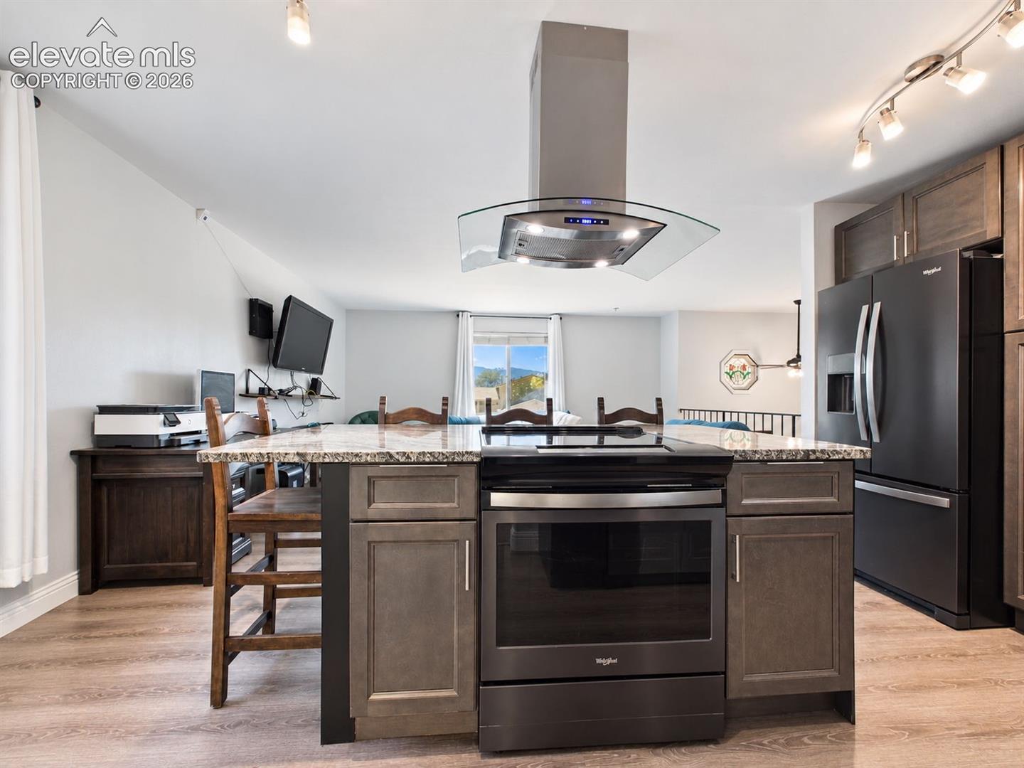 The oversized island serves as the centerpiece of the kitchen, combining the cooking area, additional cabinetry, generous counter space, and seating beneath a sleek glass-and-stainless vent hood.