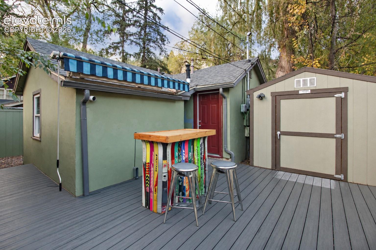 Expansive deck featuring synthetic decking boards, a retractable blue-striped awning, and a detached exterior storage structure
