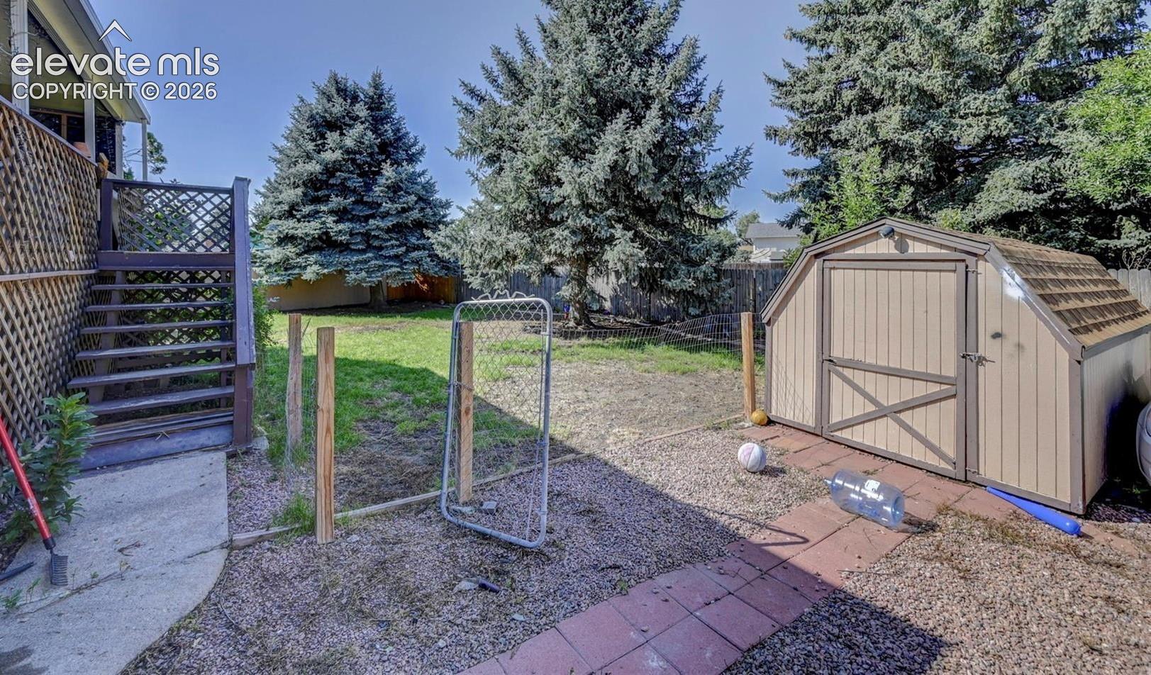 Backyard featuring a detached storage shed, exterior staircase with lattice paneling, red brick pathway, and mature evergreen trees
