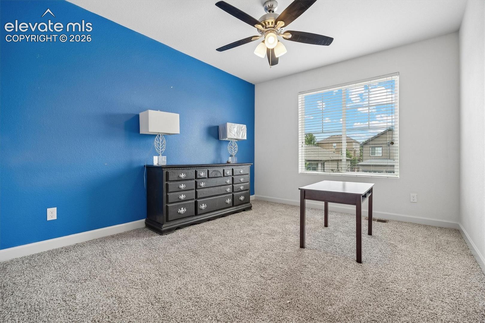 Carpeted interior space featuring a large window with horizontal blinds, a ceiling fan with integrated lighting, and a textured accent wall