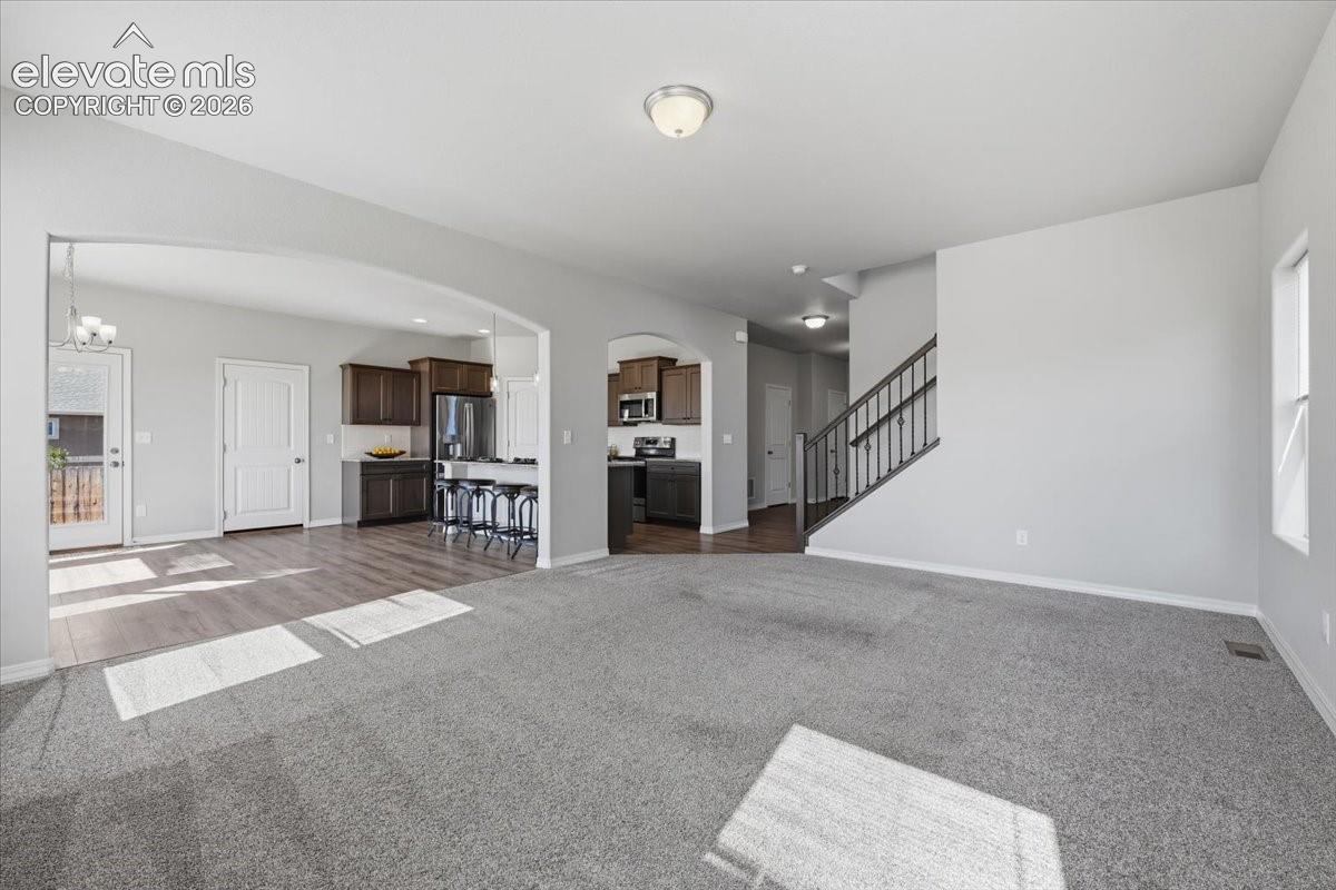Open interior featuring arched room entries, wood-finish flooring, carpeted floor surfaces, and a staircase with a metal handrail