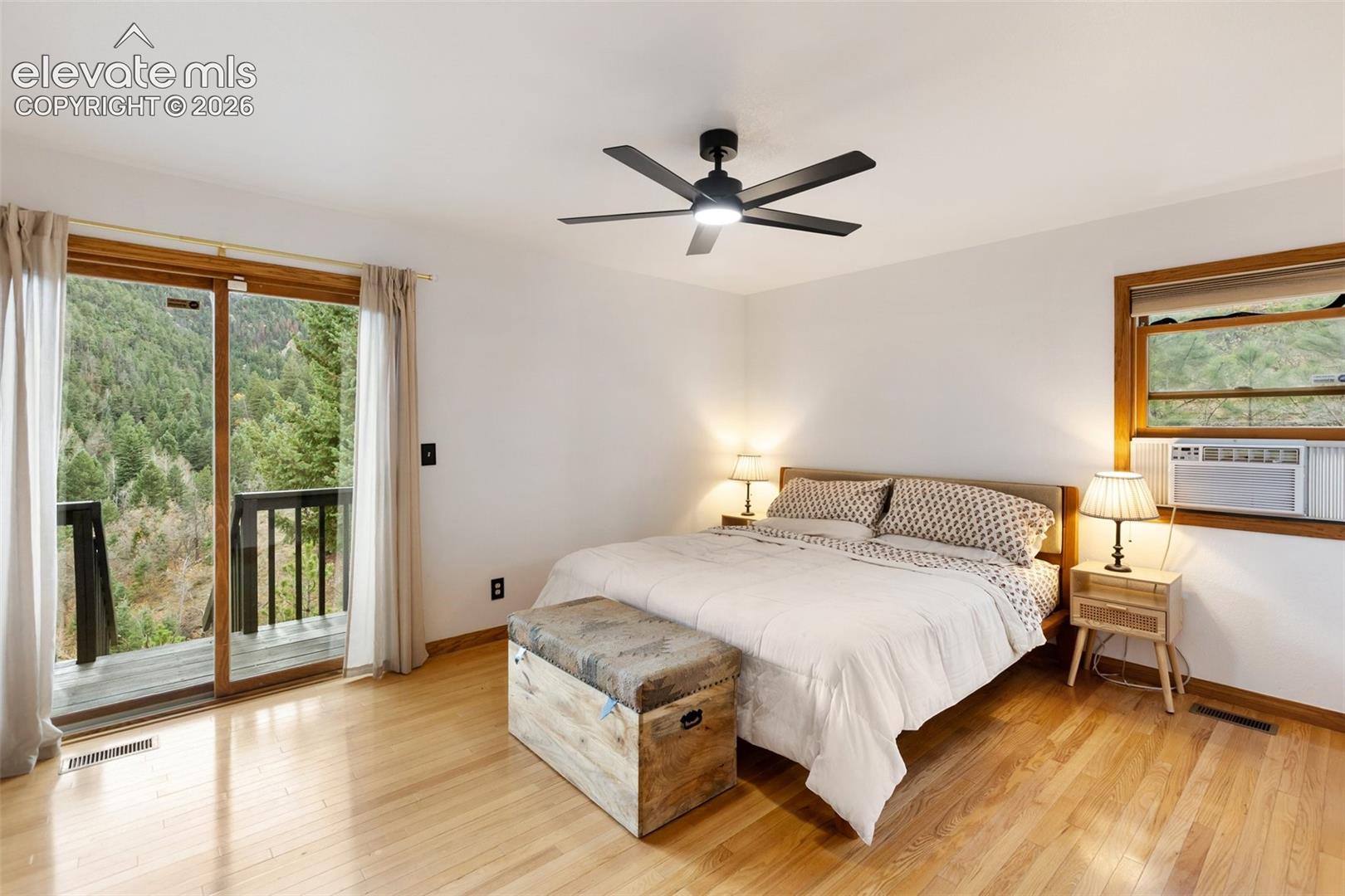 Wood-finish flooring, sliding glass door with wood-finish frame, black matte multi-blade ceiling fan with integrated lighting, and wooden window trim