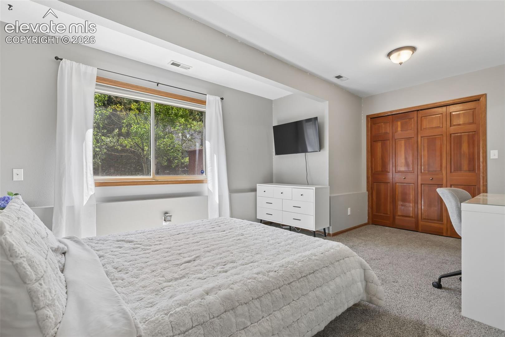 Wall-to-wall carpeting, wood-finish bi-fold doors, and a window with wood-finish trim