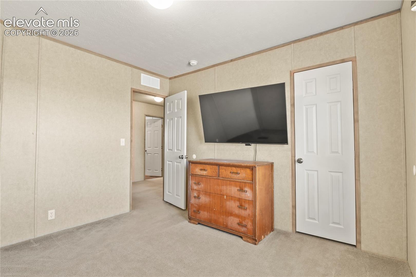 Interior space featuring textured wall panels, neutral carpeting, and white six-panel interior doors with brass-finish hardware