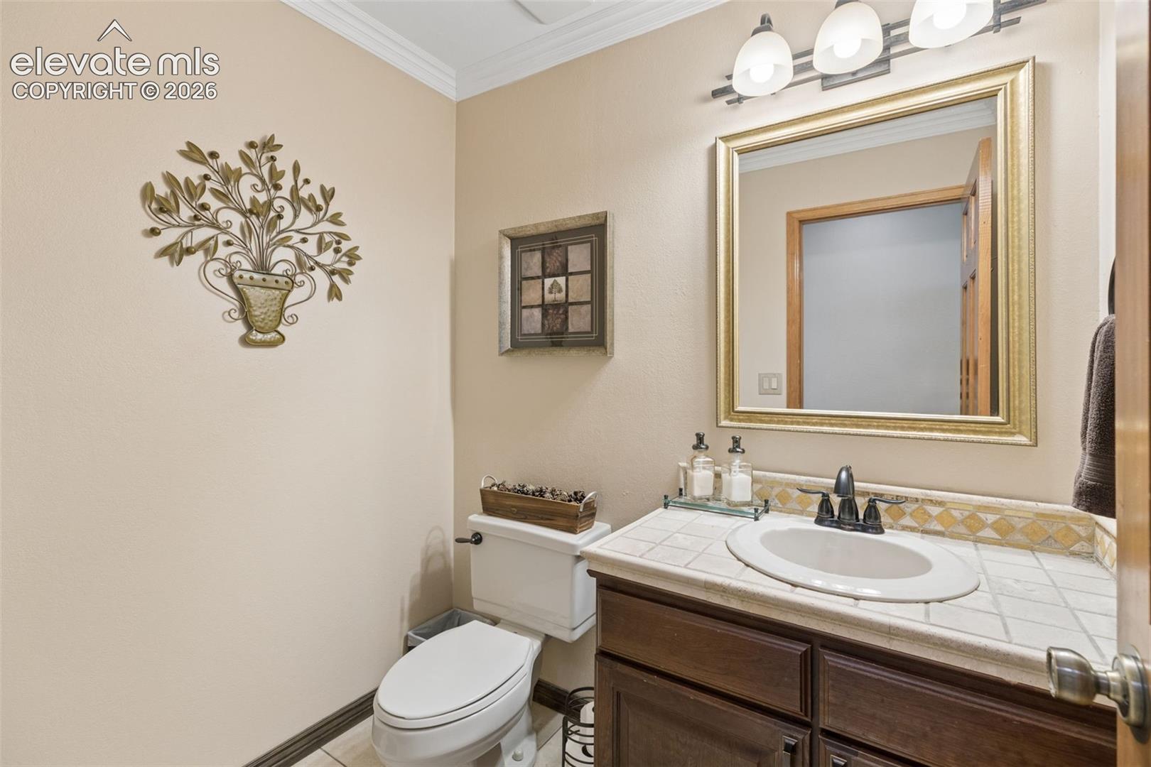 Restroom featuring a dark wood-finish vanity, tiled countertop with an integrated oval sink, decorative tile backsplash, and a three-light fixture above a framed mirror