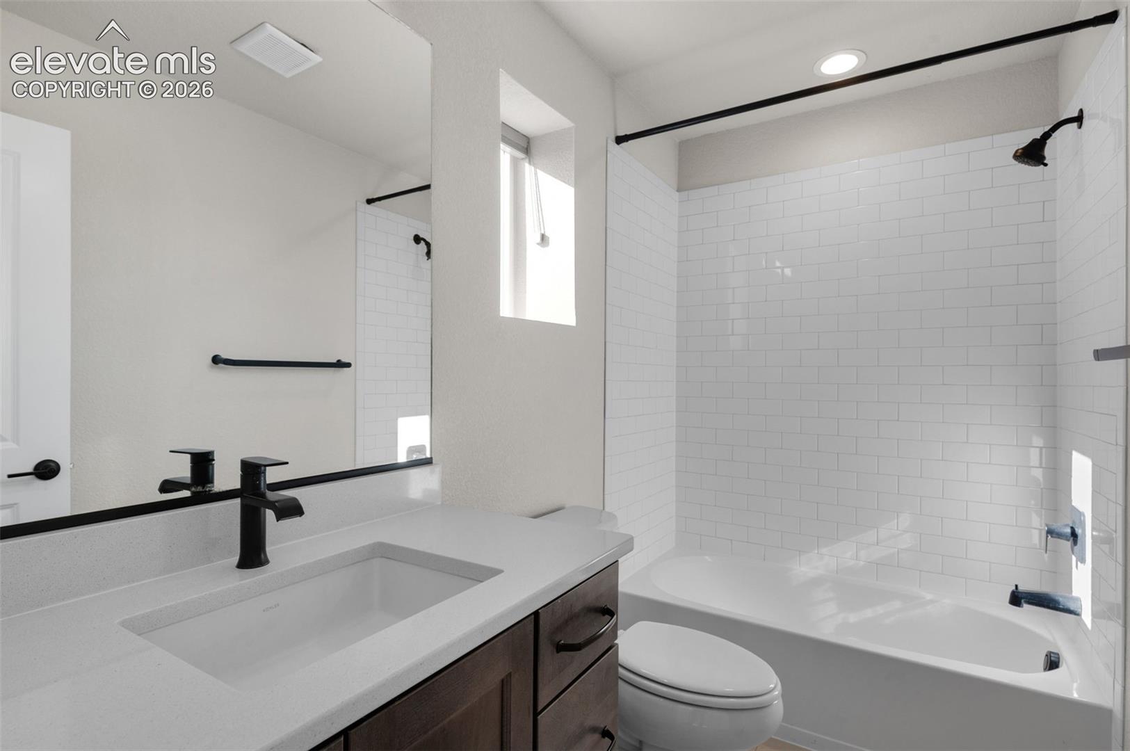 Bathroom featuring a single vanity with an integrated sink, dark wood-finish cabinetry, a white subway tile shower surround, and matte black fixtures