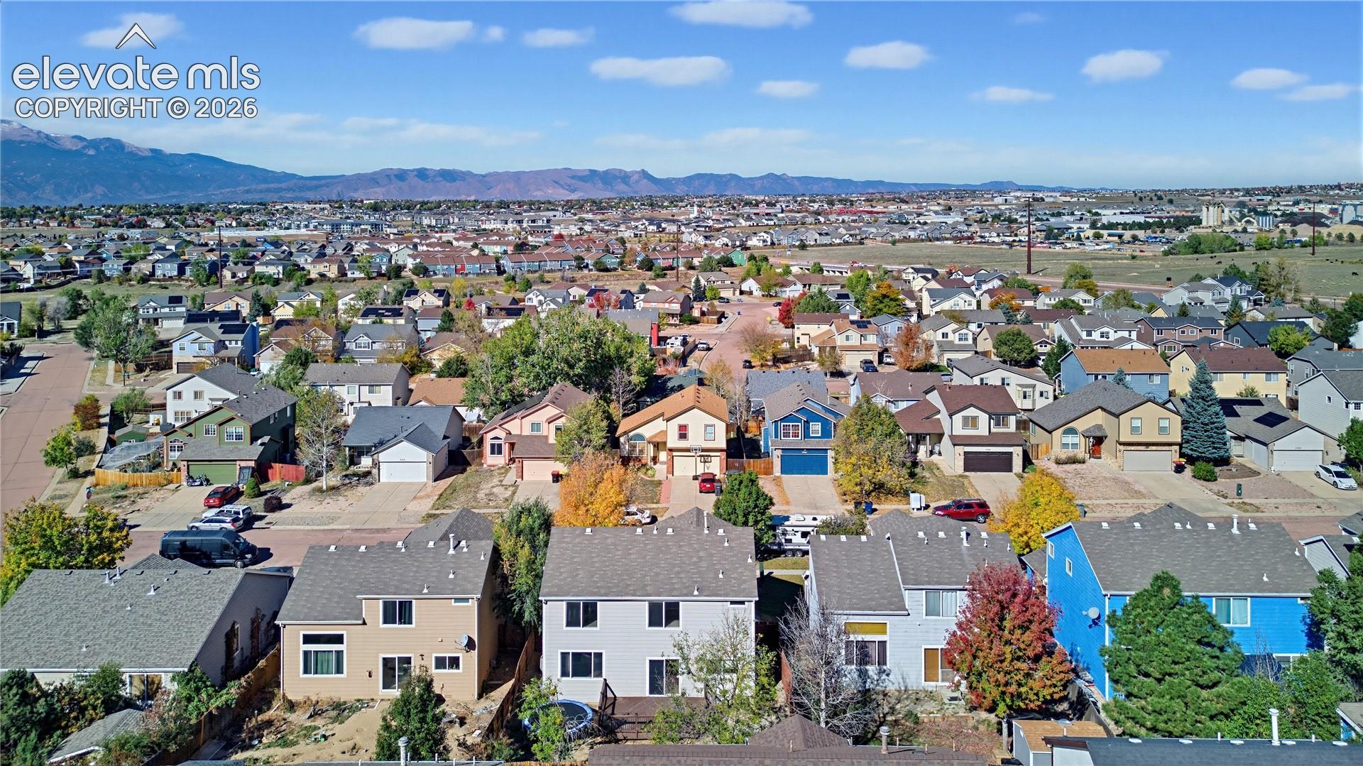 Aerial perspective of a suburban neighborhood featuring residential homes, mature deciduous trees, and a distant mountain range backdrop
