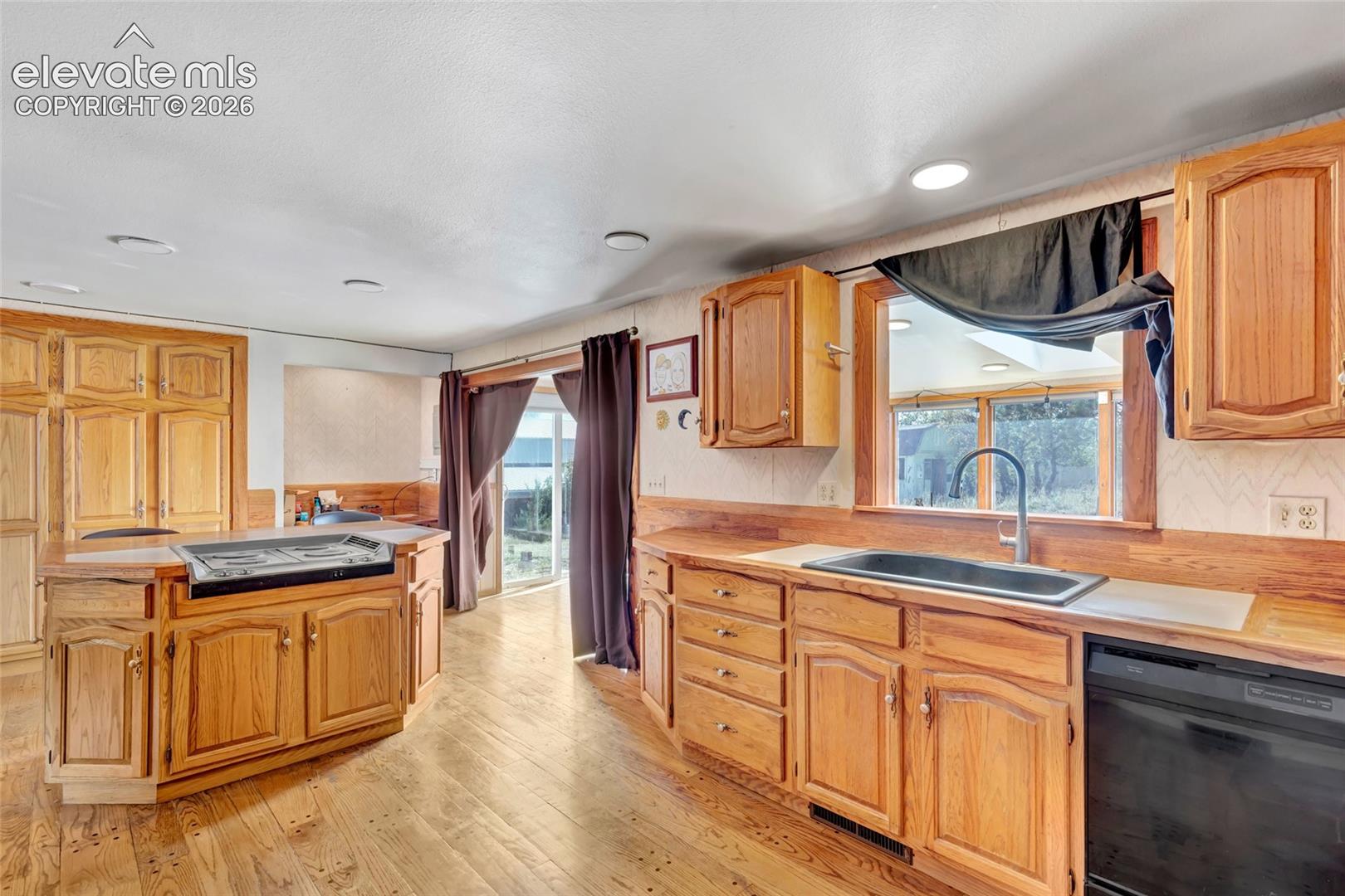 Wood-finish flooring, wood cabinetry, and a kitchen island with a built-in cooktop