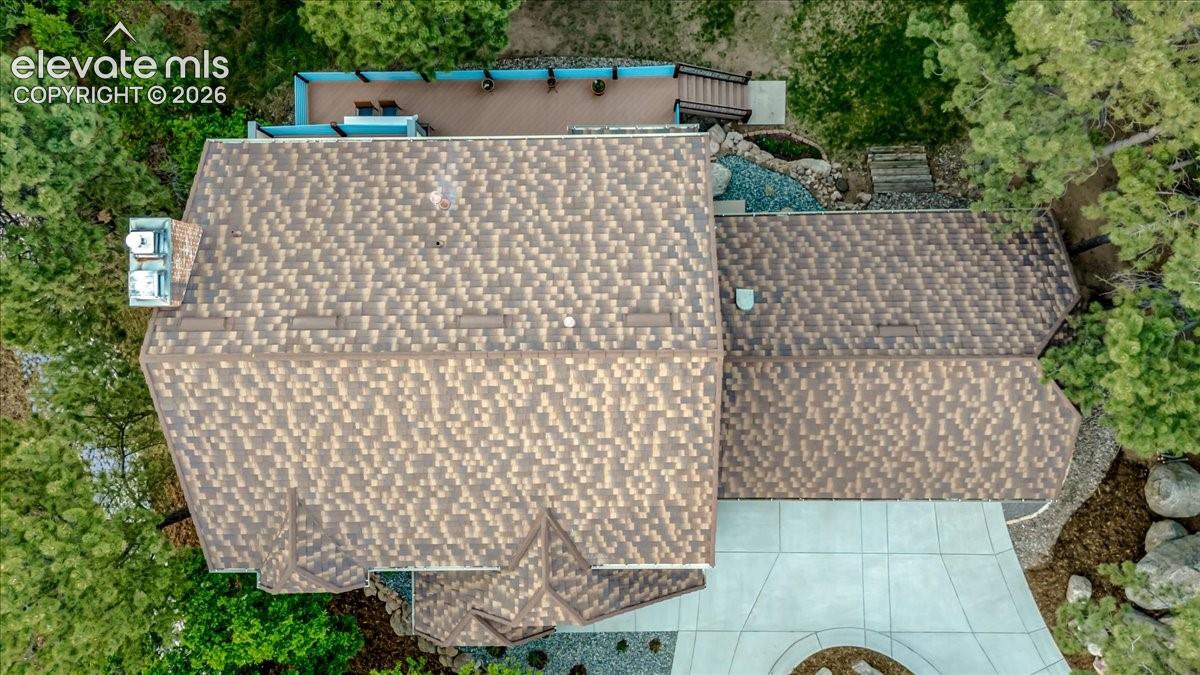  stone coated steel roofing with varied tones, multiple rooflines, a multi-level outdoor deck, and established perimeter trees