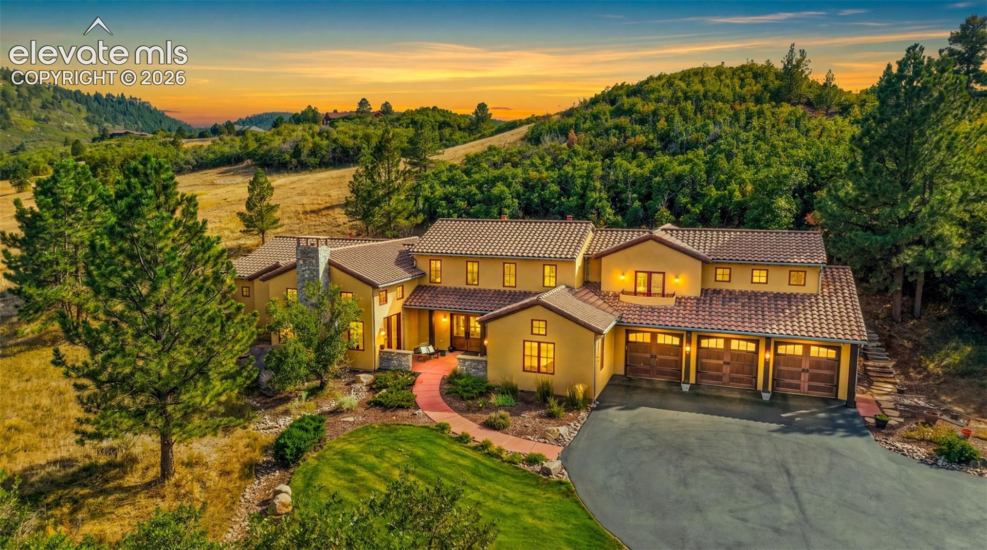 Stucco exterior residence featuring a tile roof, multi-car garage with wood-finish doors, and a paved driveway