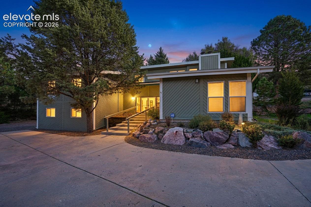 Exterior facade featuring diagonal wood-style siding, multi-level roofline, concrete driveway, stone rockery landscaping, and a tiered staircase entrance