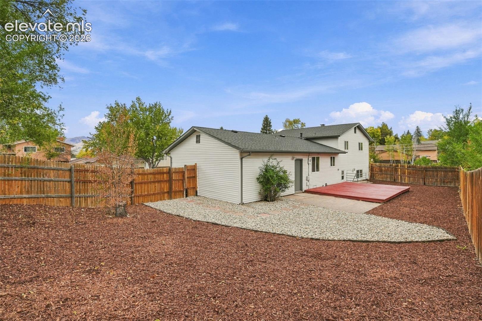 Backyard featuring a raised wooden deck, partial gravel landscaping, perimeter wood fencing, and horizontal siding
