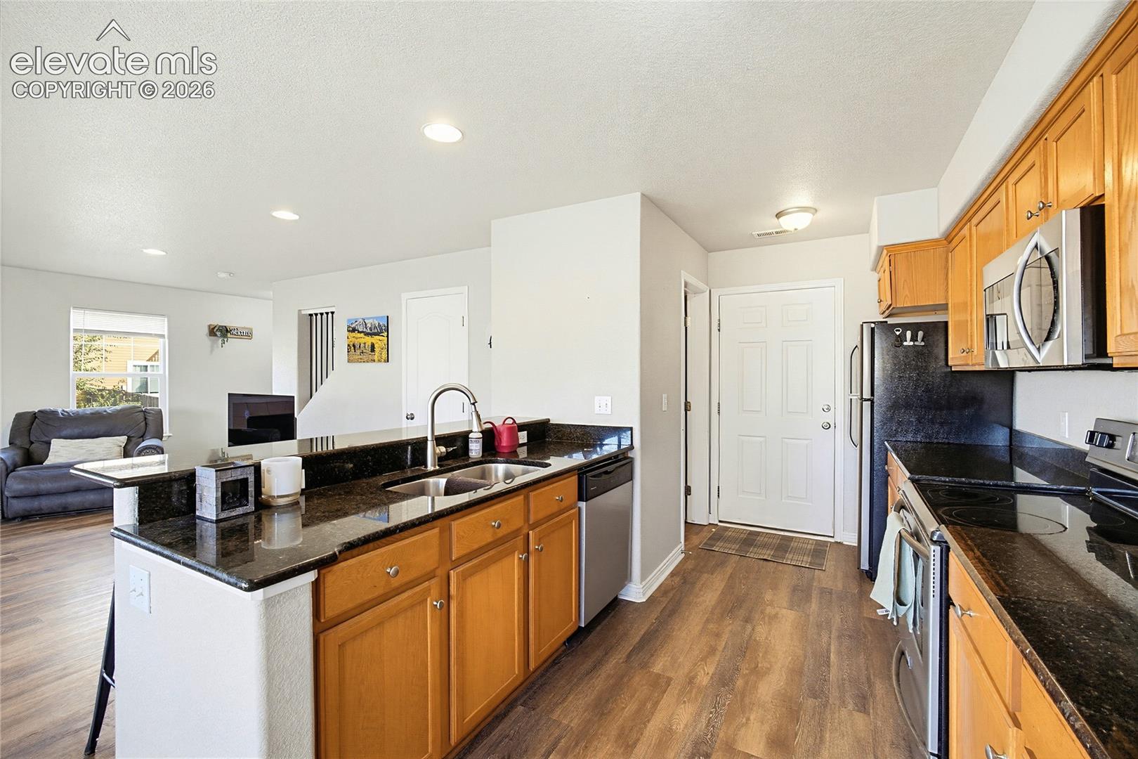 Kitchen featuring wood cabinetry, dark stone countertops, stainless steel appliances, a double-basin sink with a gooseneck faucet, and wood-finish flooring