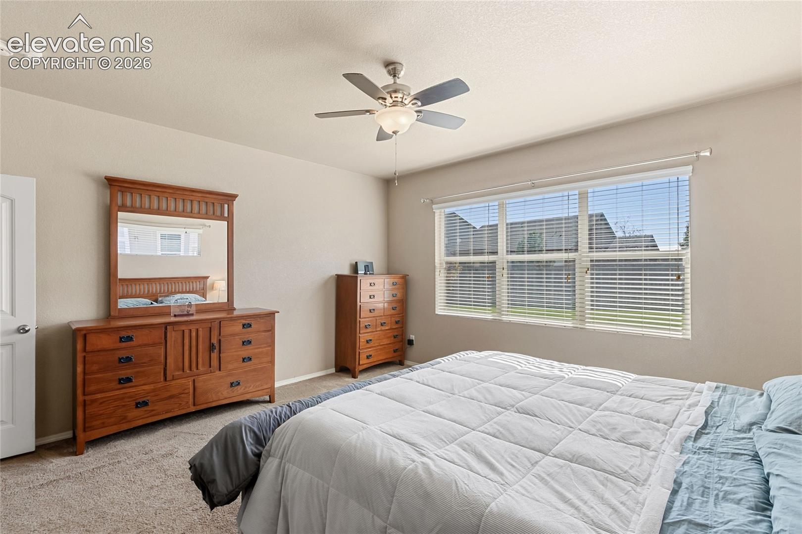 Spacious room featuring neutral carpeting, a central ceiling fan with integrated lighting, and a large multi-pane window with installed blinds