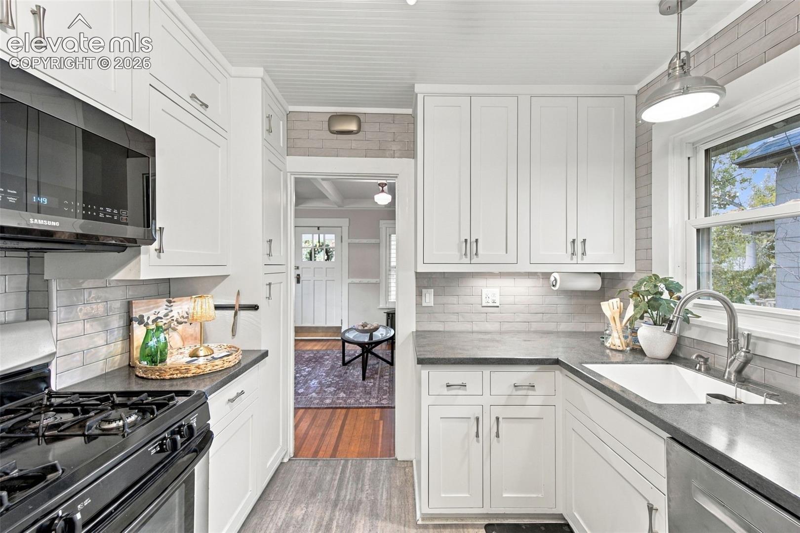 Kitchen featuring white cabinetry, grey subway tile backsplash, dark solid-surface countertops, beadboard ceiling, and a stainless steel undermount sink
