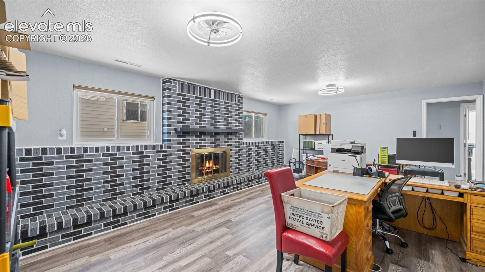 Spacious room featuring a prominent fireplace with a mosaic tile surround and hearth, wood-finish flooring, two windows, and recessed lighting fixtures
