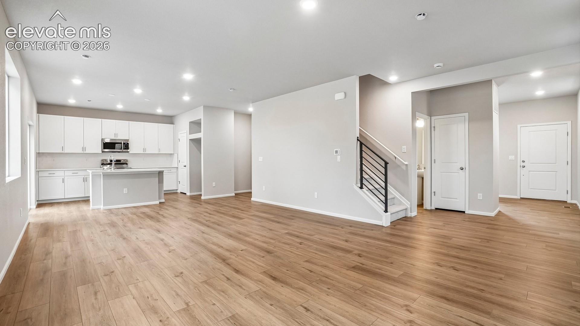 Open-concept living space featuring wood-finish flooring, recessed lighting, and a kitchen with white cabinetry and a central island
*photos of a model home*
